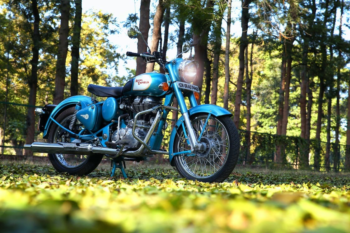A blue motorcycle parked in a field, showcasing its vibrant color against the serene backdrop of nature.