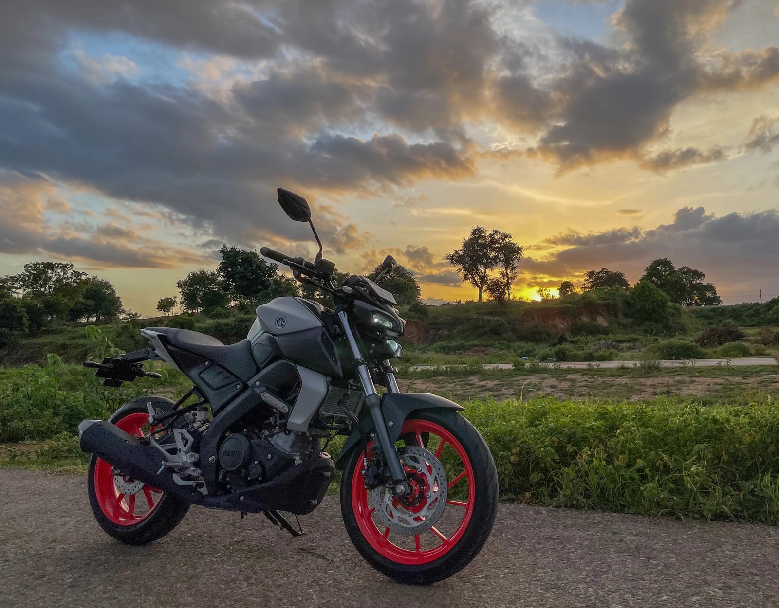 A parked motorcycle on the road, with the sun setting behind it, casting a warm glow.